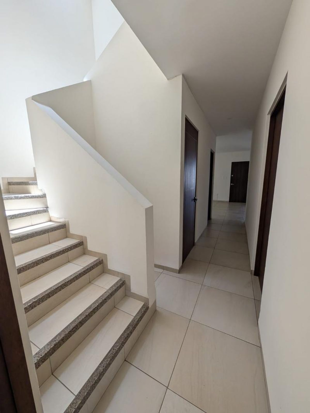 Pasillo con piso de cerámica clara, escaleras de granito y puertas de madera oscura