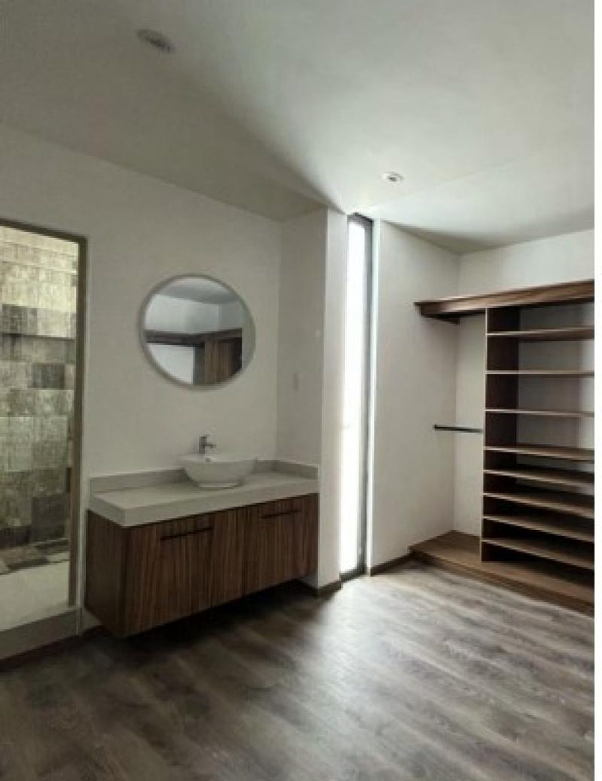 Mueble de baño de madera con lavabo, espejo redondo y vestidor con repisas