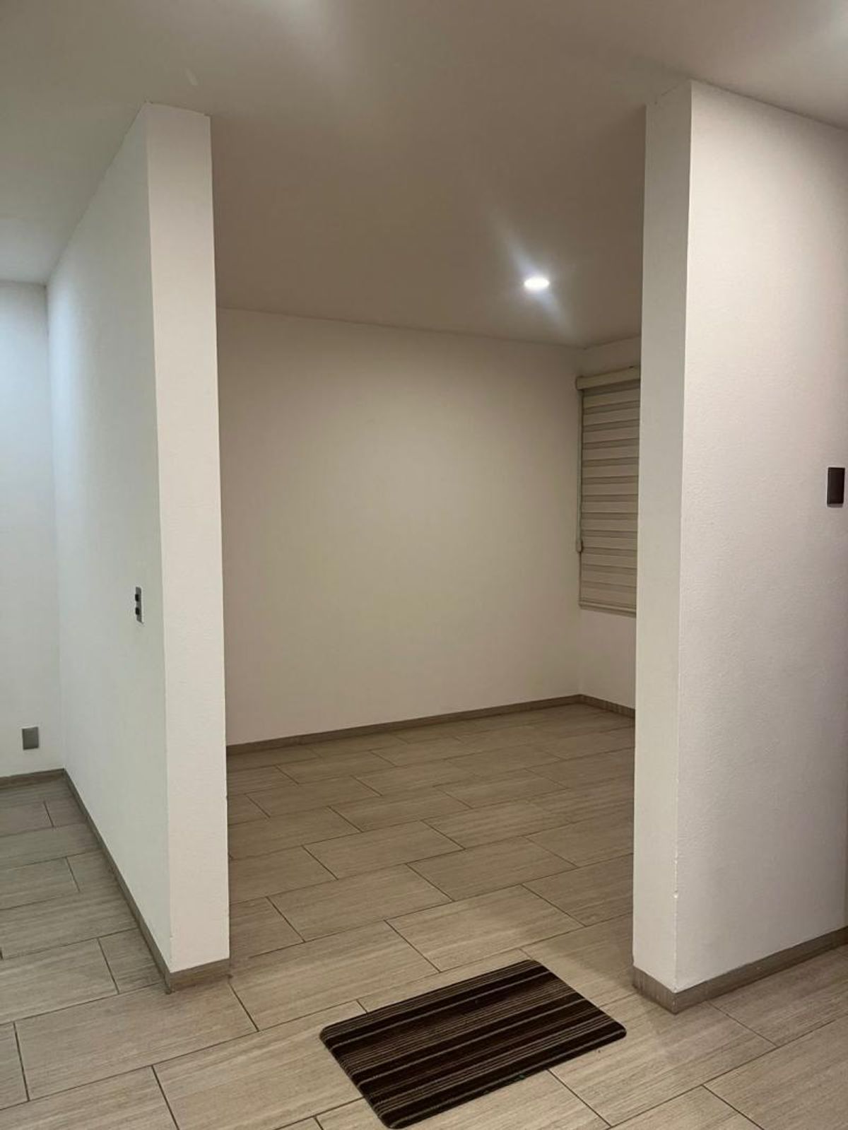 Espacio vacío con paredes blancas, piso cerámico tipo madera y ventana con persiana