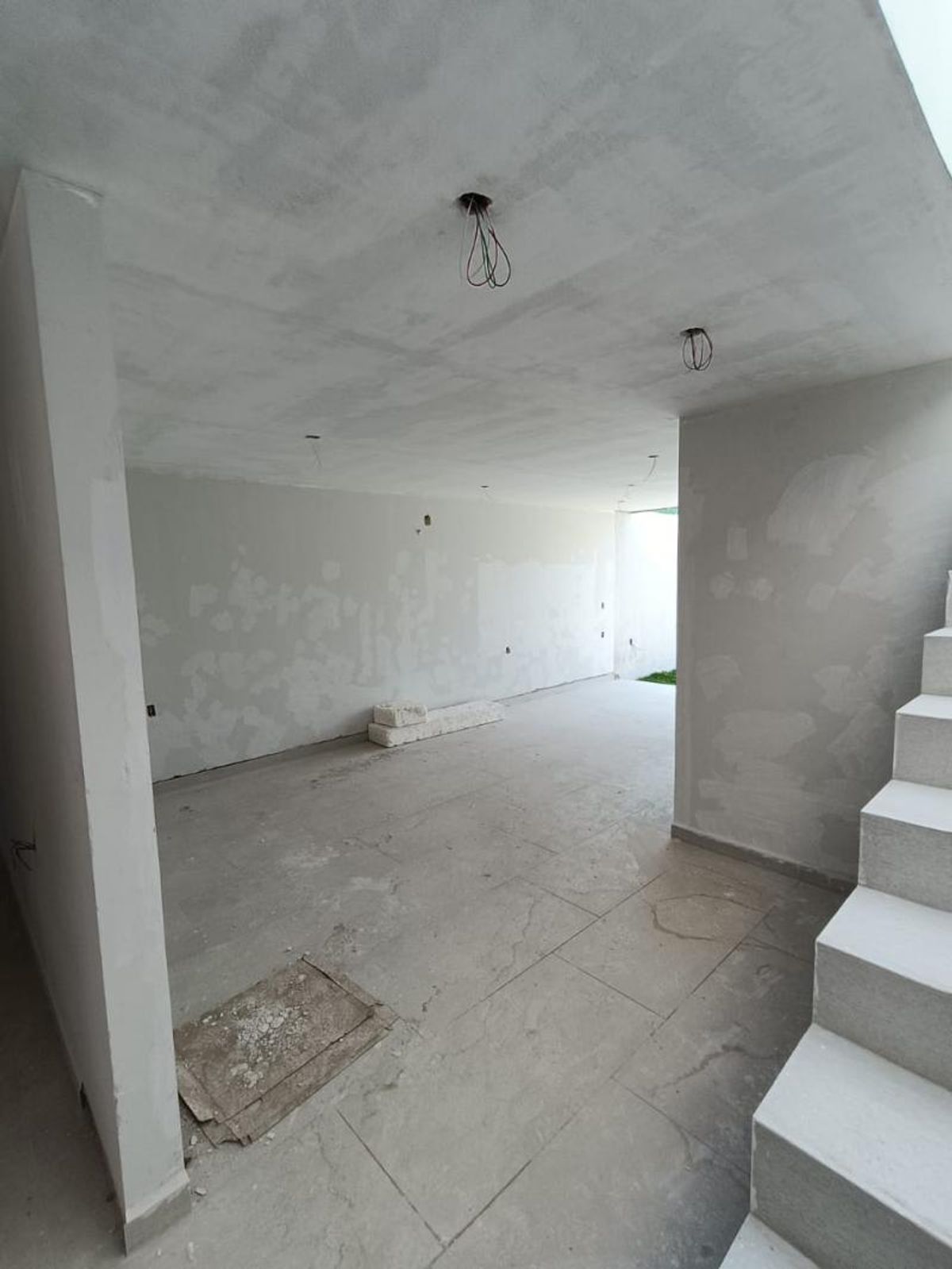 Habitación interior vacía con paredes blancas, piso de loseta gris y escalera lateral