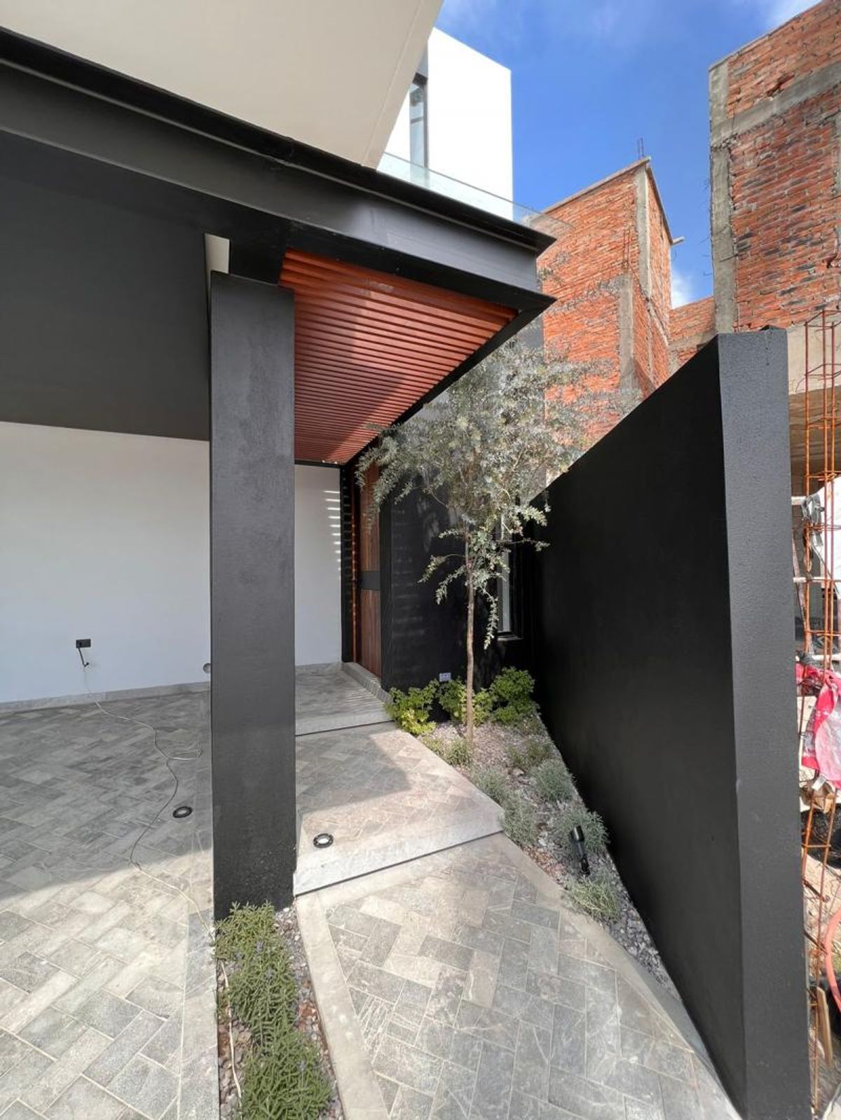 Acceso principal con piso de adoquín gris, plafón de listones de madera y jardinería