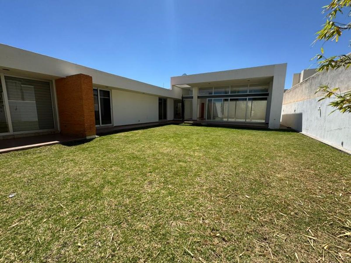 Jardín de césped verde junto a casa blanca de un piso con grandes ventanales