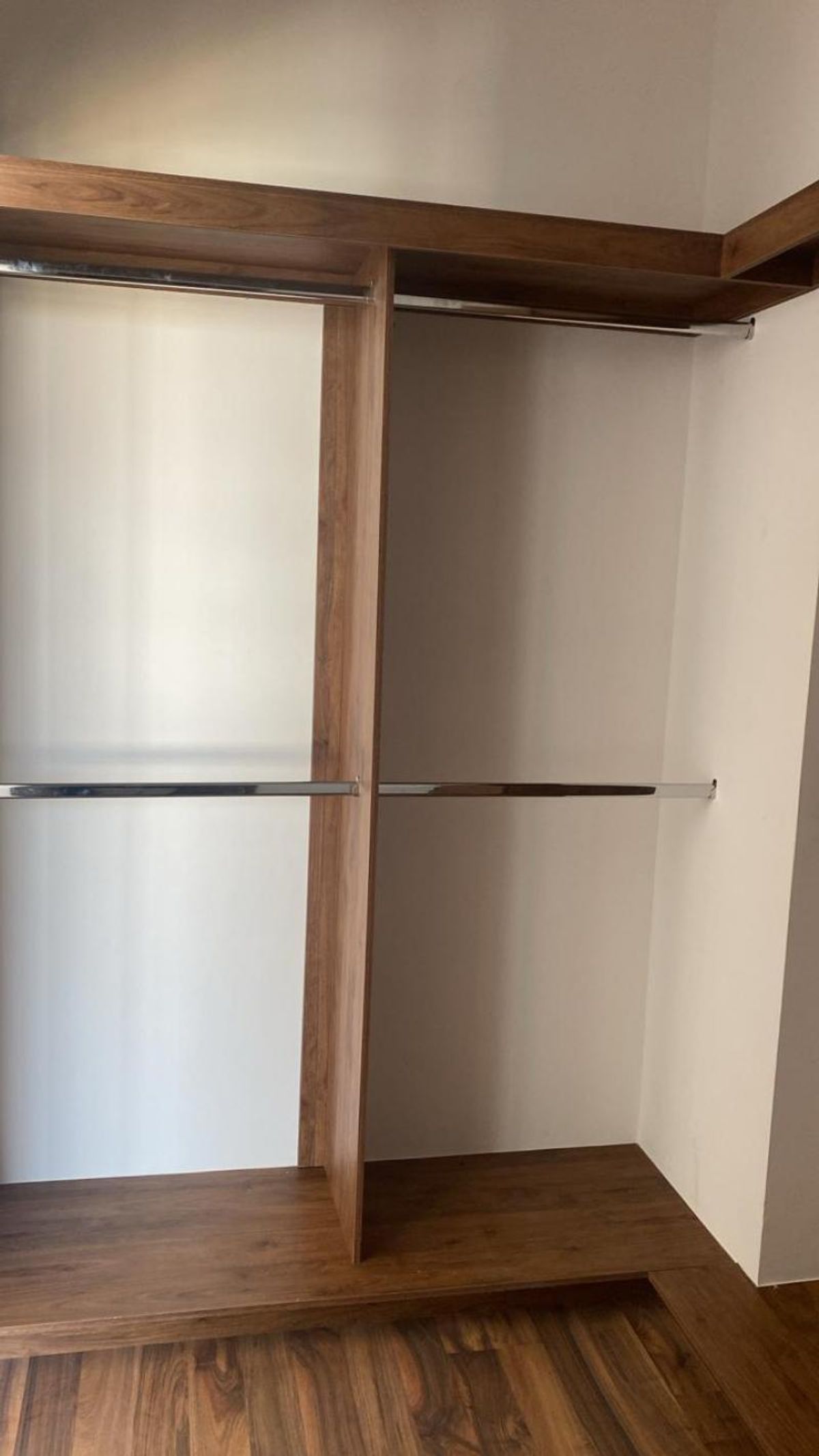 Clóset de madera con divisiones verticales, repisas horizontales y barras metálicas para colgar