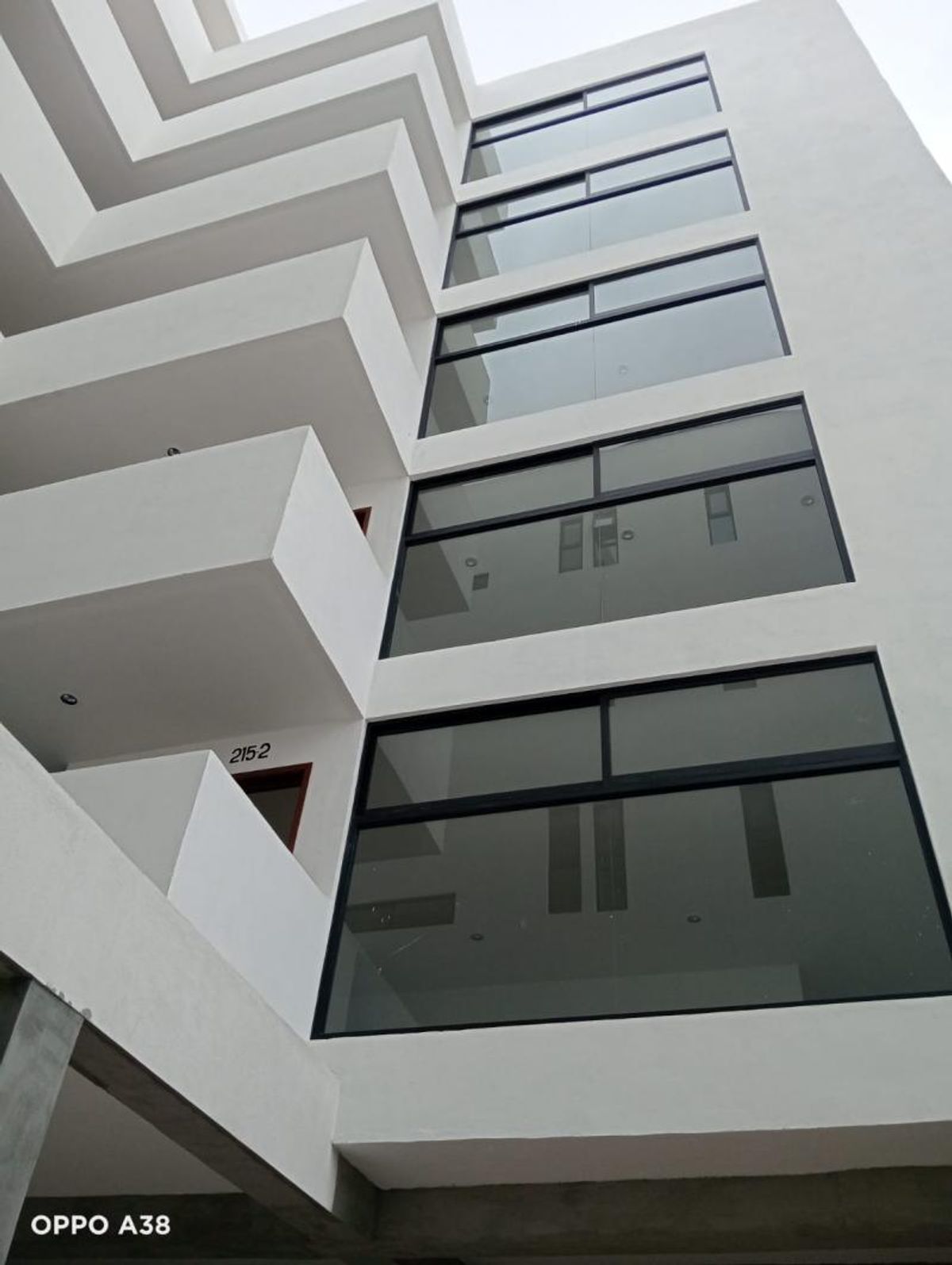 Fachada blanca de edificio de departamentos con balcones y grandes ventanales con marcos negros