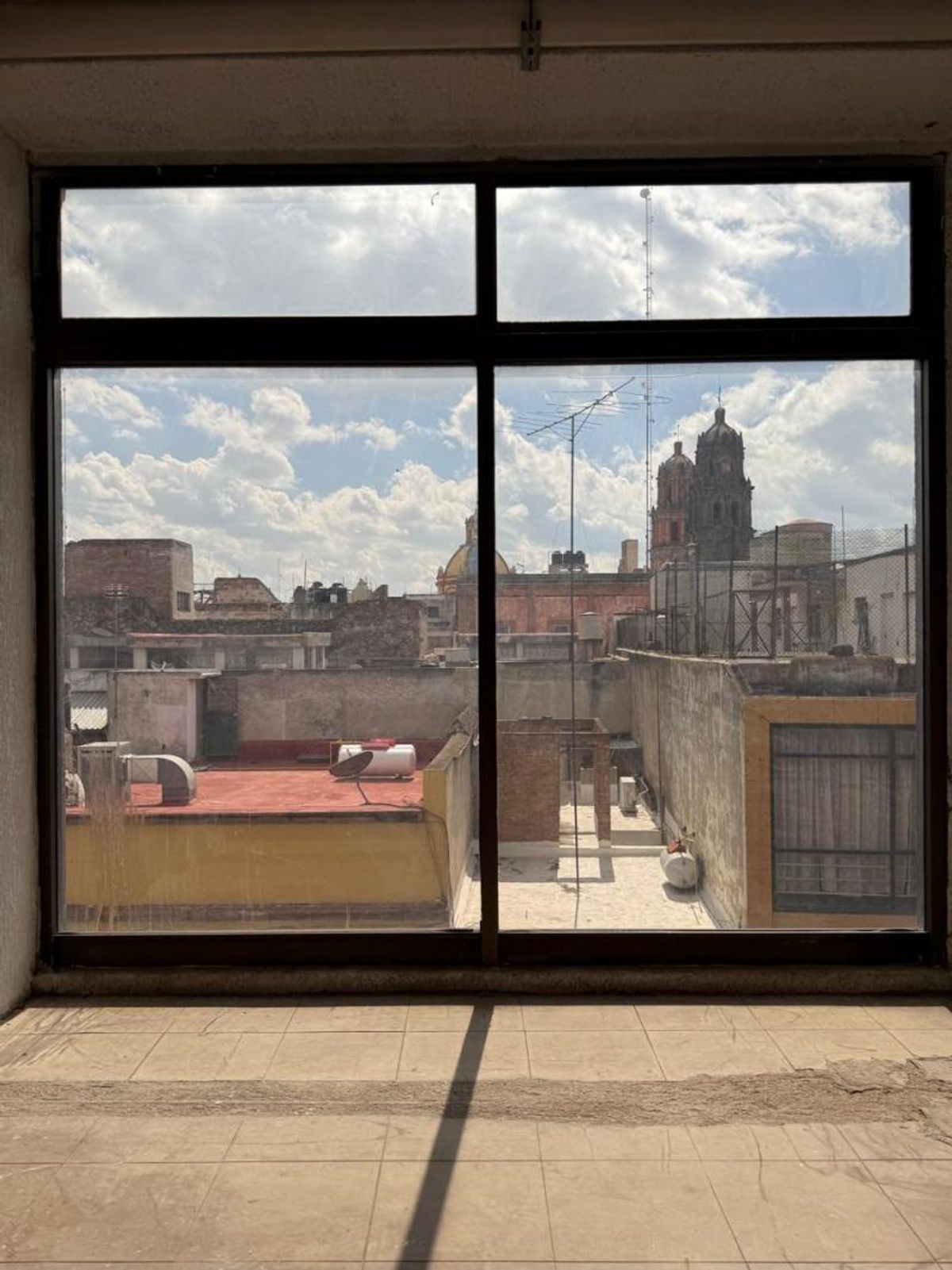 Espacio con piso de baldosa y gran ventanal de marco negro hacia azoteas urbanas