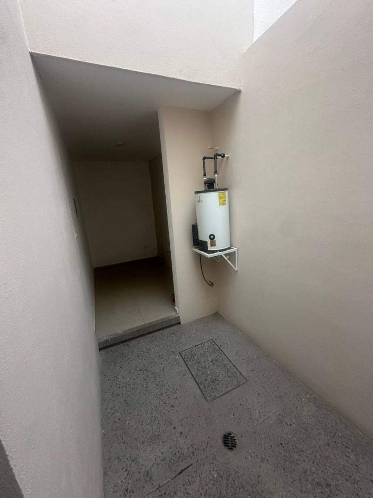 Patio de servicio con calentador de agua en pared y piso de concreto gris
