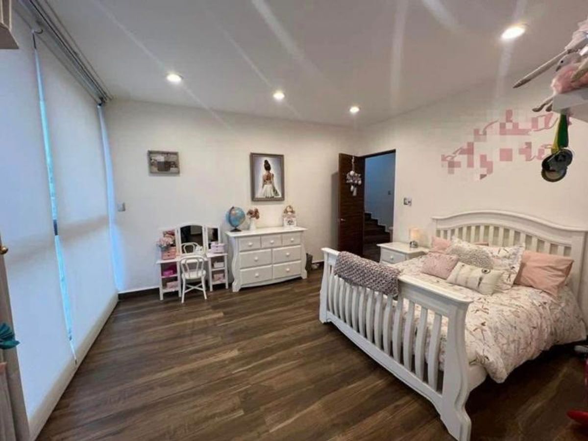 Recámara infantil con cama blanca, tocador, cómoda y piso de madera en tono oscuro