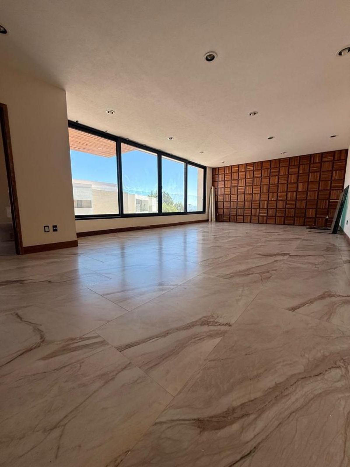 Sala vacía con piso de porcelanato veteado, grandes ventanales y pared decorativa de madera