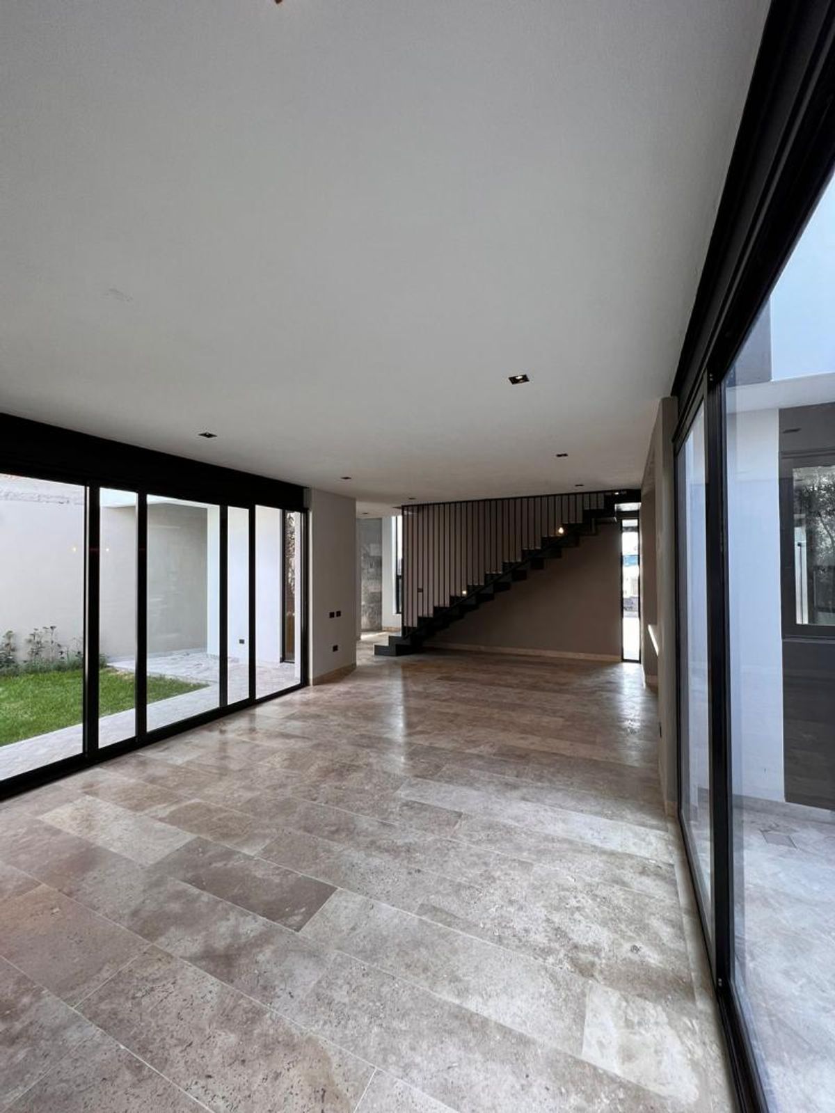 Espacio abierto con piso de mármol travertino, ventanales de cristal y escalera metálica negra