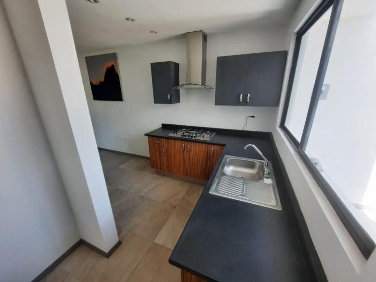 Cocina con cubierta negra, gabinetes de madera, tarja de acero inoxidable y campana extractora