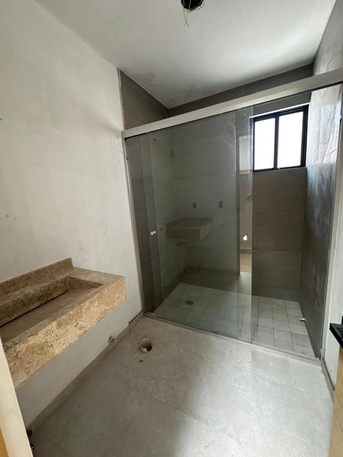 Baño con lavabo flotante de mármol travertino y regadera con cancel de cristal