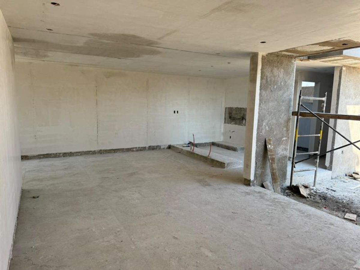 Espacio interior amplio en obra gris con muros aplanados, piso de concreto y andamio