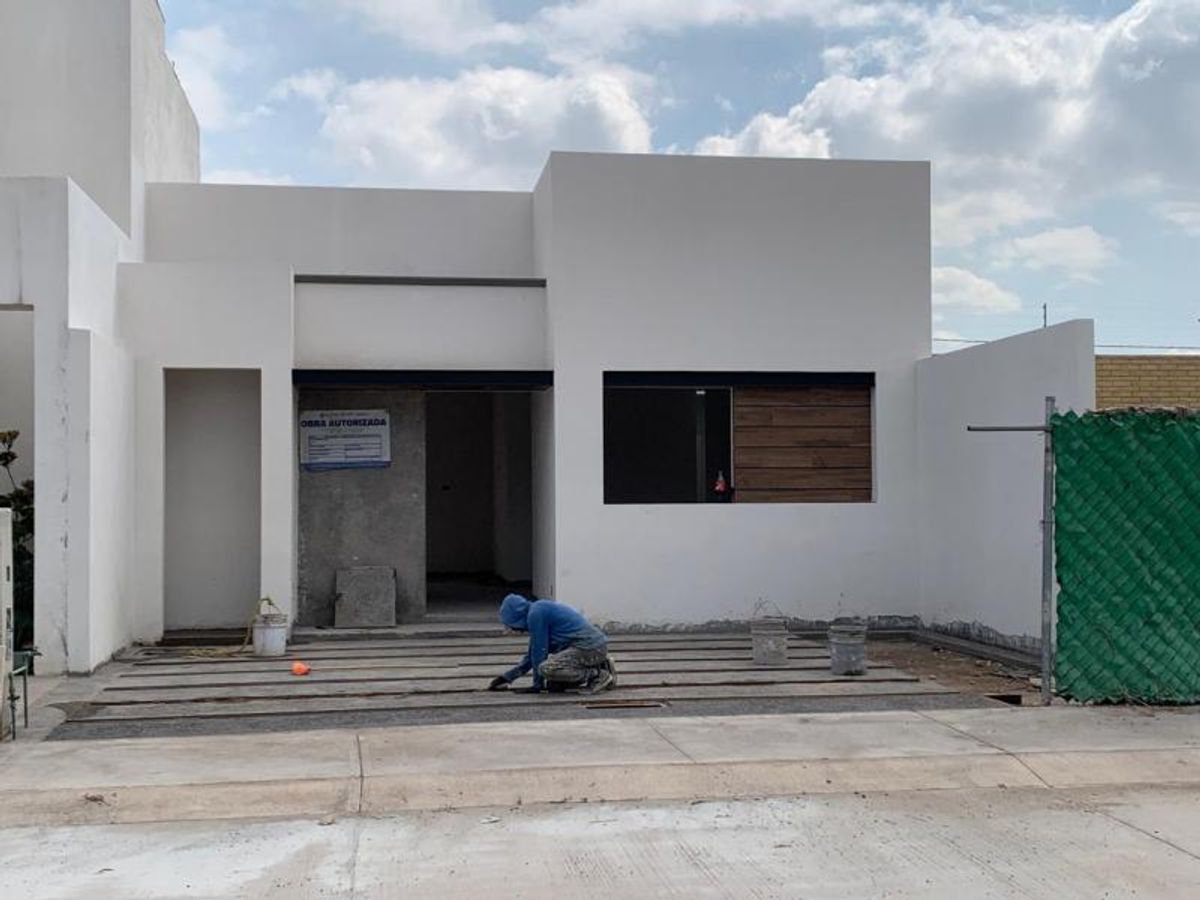 Fachada blanca de una planta con acento de madera en ventana y cochera en construcción