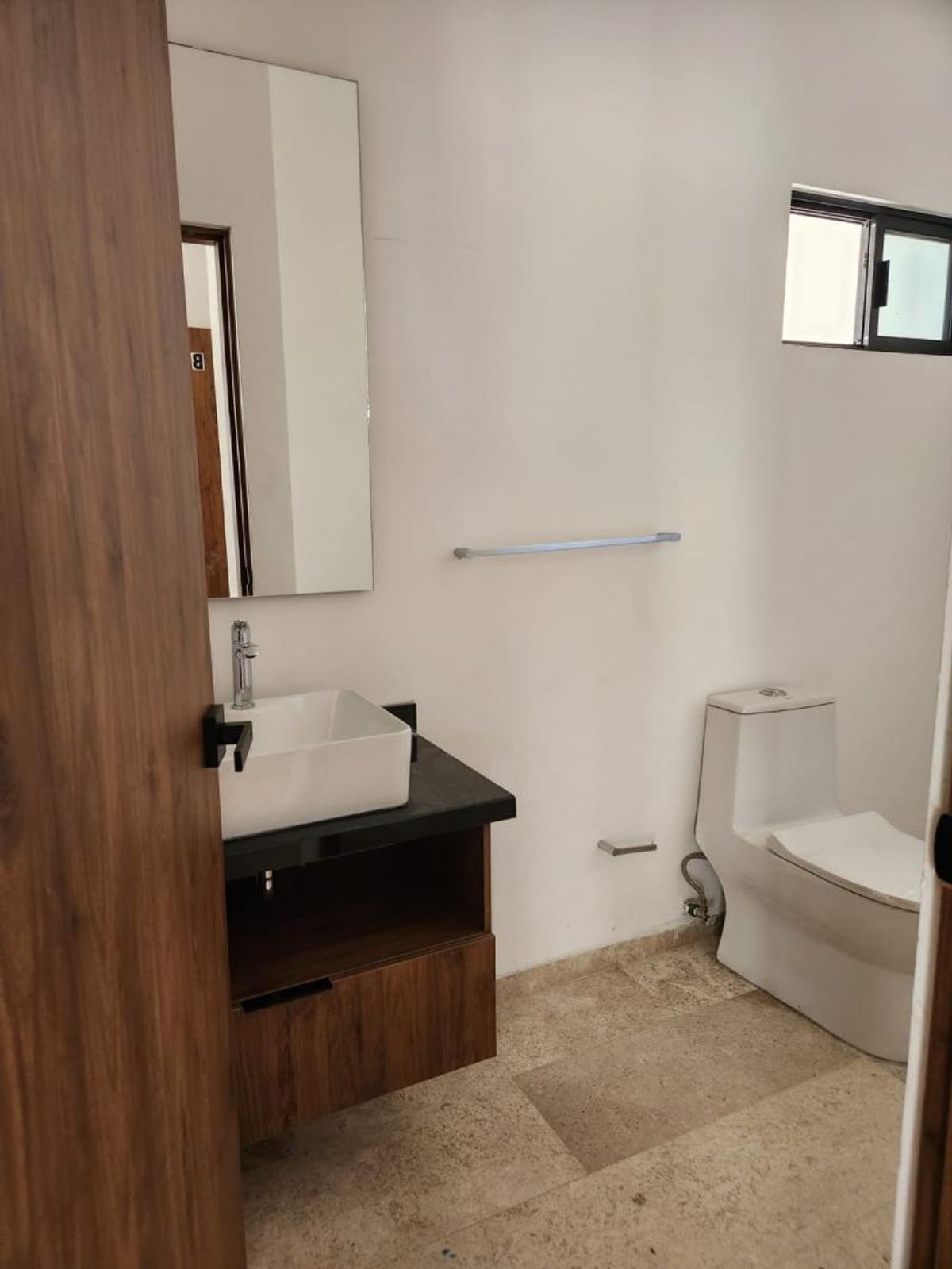 Baño con lavabo de sobreponer en mueble de madera, espejo vertical e inodoro blanco