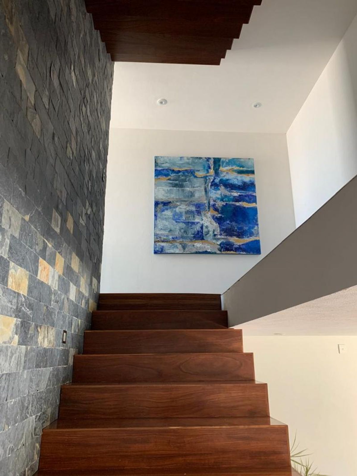 Escalera de madera oscura junto a pared de piedra gris y pintura abstracta azul