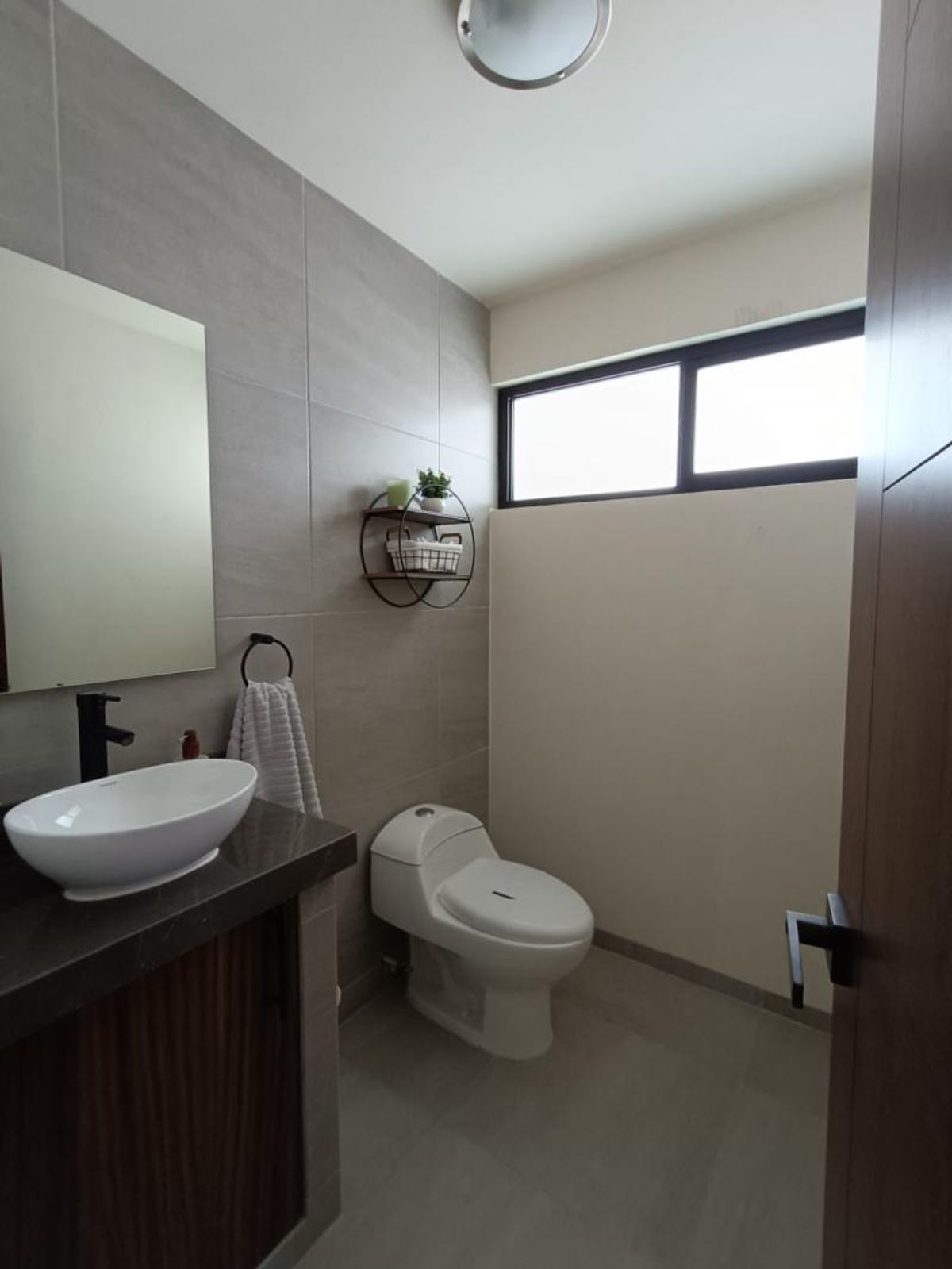 Medio baño con lavabo ovalado blanco, grifo negro, inodoro y paredes de azulejo gris