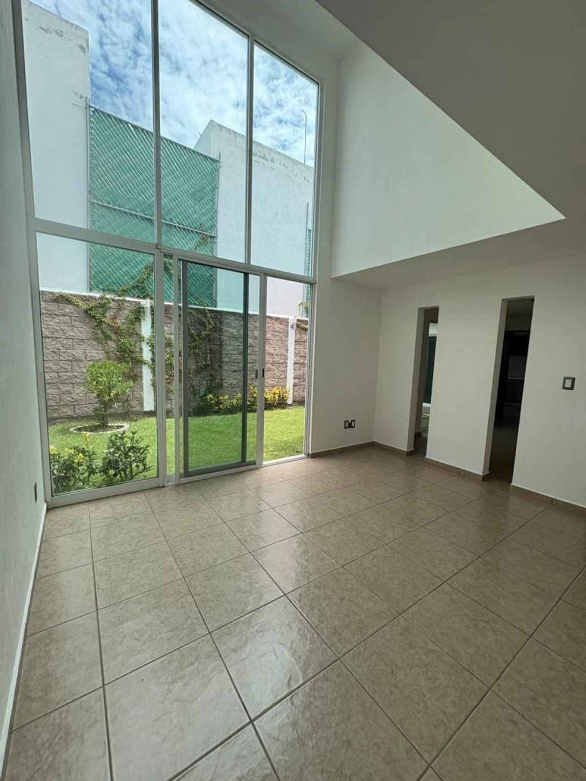 Espacio de doble altura con piso de cerámica y ventanal con vista al jardín