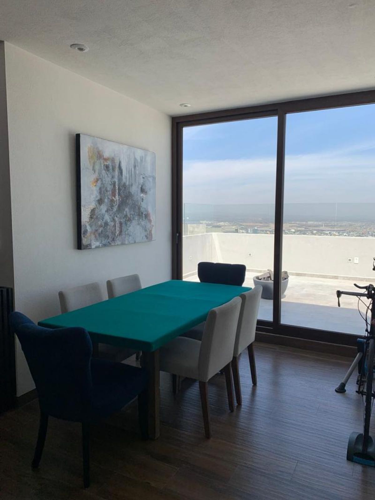 Comedor con mesa verde, sillas tapizadas y gran ventanal hacia la terraza con vista
