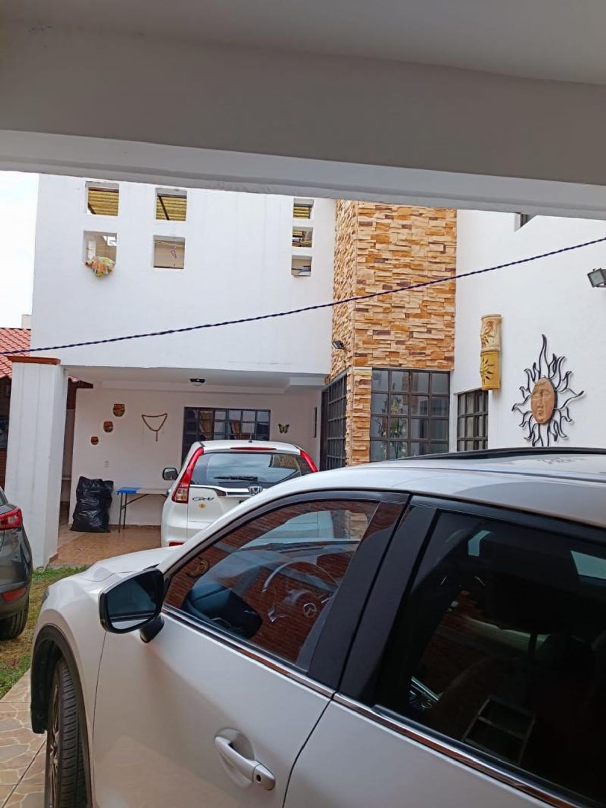 Fachada de casa blanca con revestimiento de piedra y cochera techada con vehículos