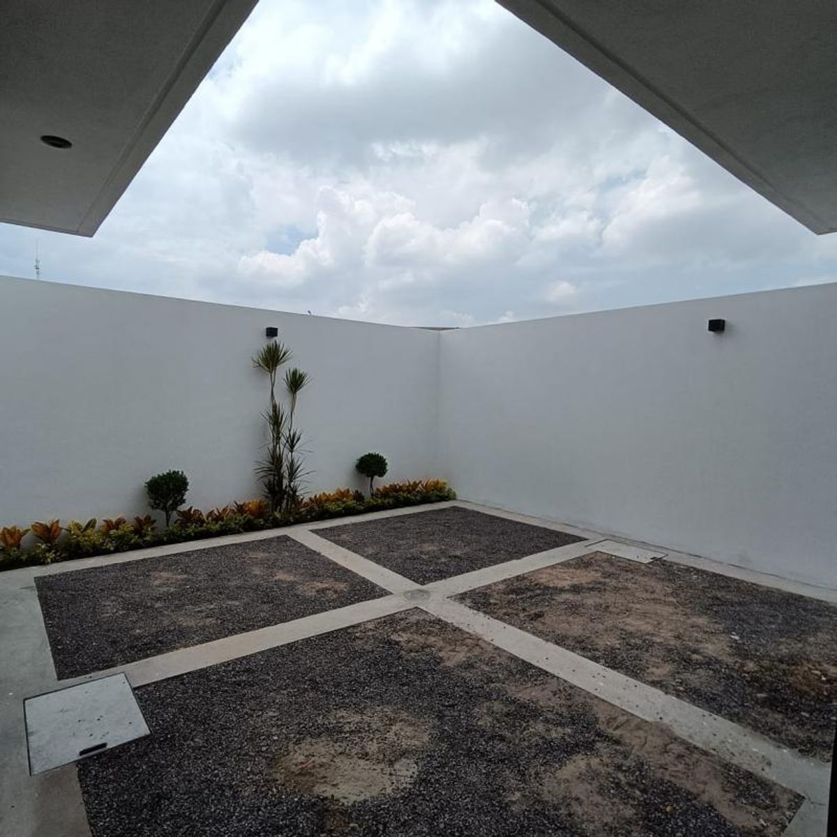 Patio descubierto con piso de grava en cuadrícula de concreto, muros blancos y jardinería