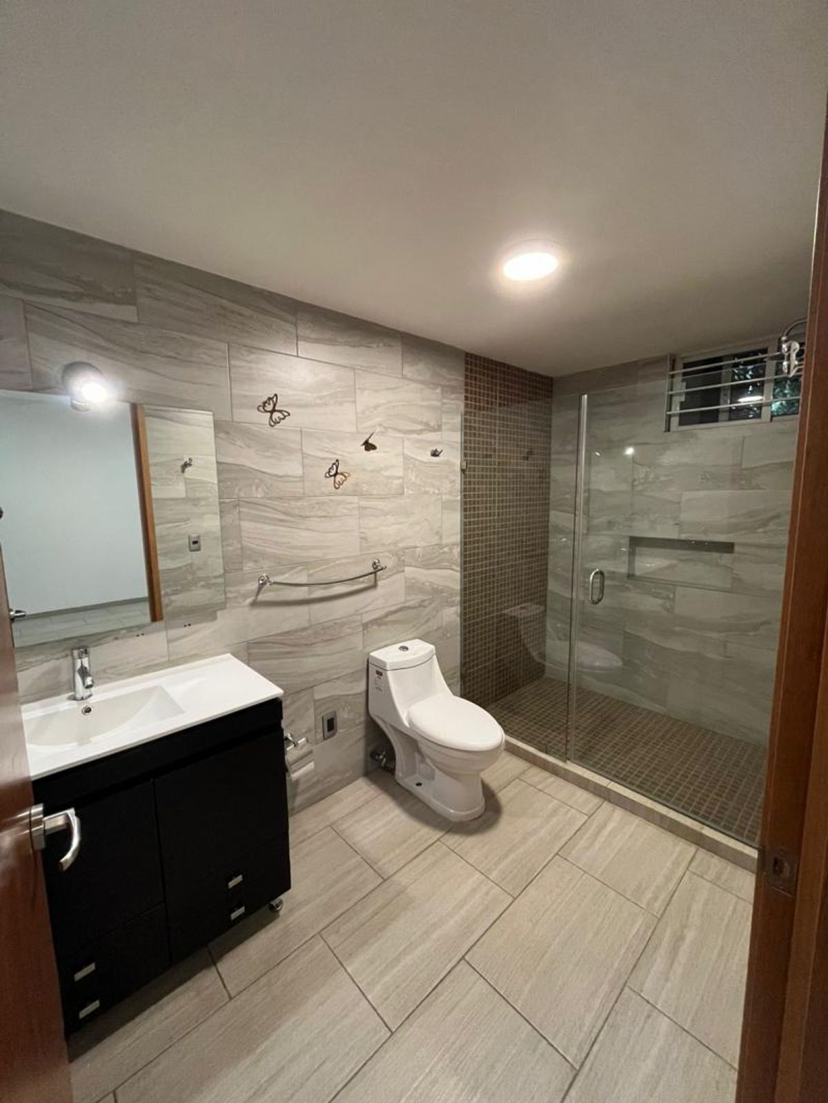 Baño con mueble de lavabo negro, inodoro blanco y regadera con cancel de cristal
