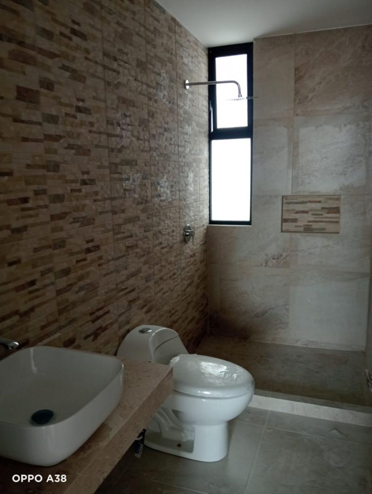 Baño con lavabo cerámico sobre cubierta, inodoro blanco y área de regadera con ventana