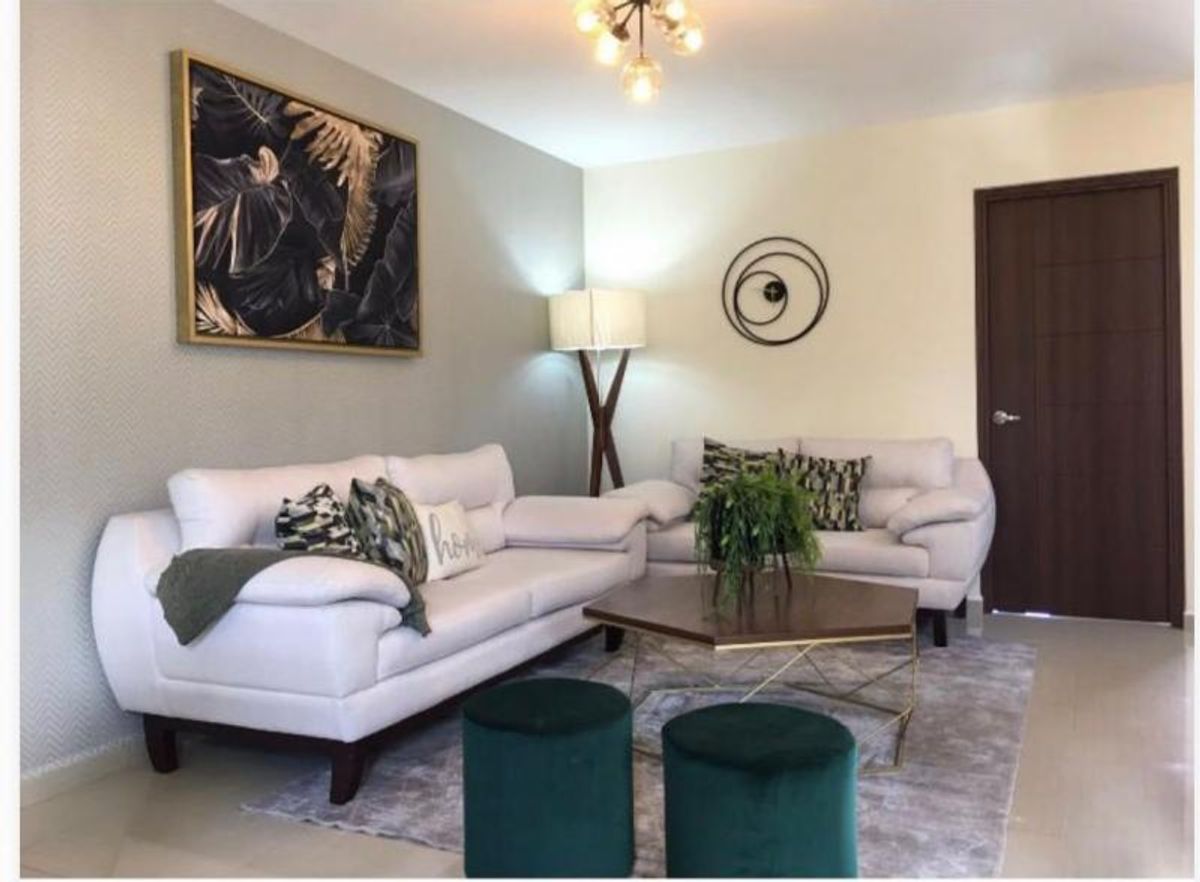 Sala de estar con sofás claros, mesa de centro hexagonal, taburetes verdes y cuadro decorativo