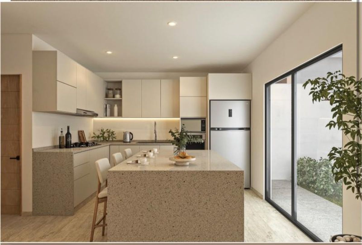 Cocina integral con isla de granito beige, gabinetes claros, refrigerador y ventanal al patio