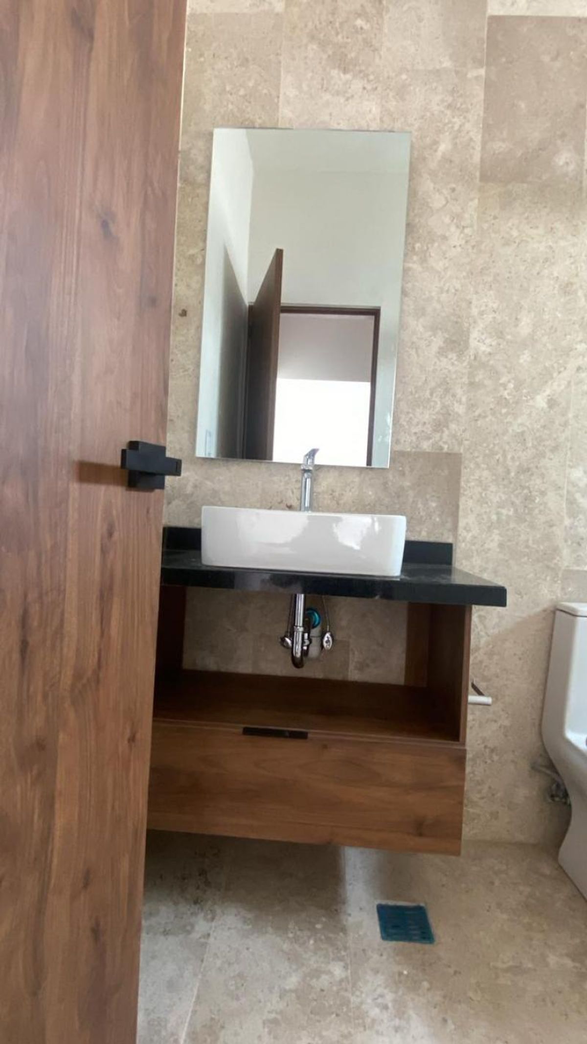 Baño con lavabo blanco sobre cubierta negra, mueble flotante de madera y revestimiento beige