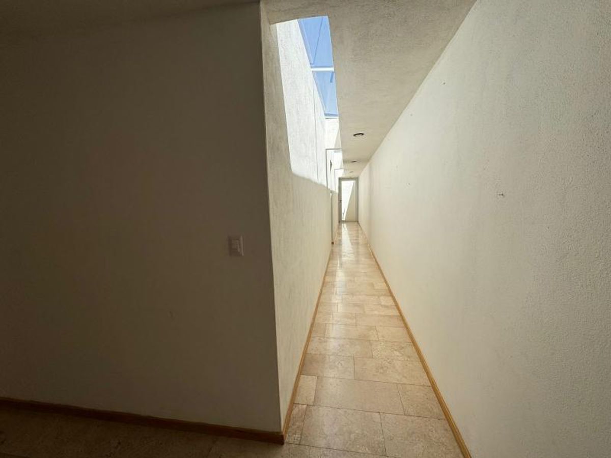 Pasillo largo con piso de mármol claro, paredes blancas y tragaluz de iluminación natural