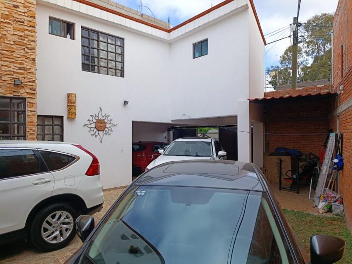 Patio y cochera con fachada blanca de dos niveles, detalles en piedra y vehículos