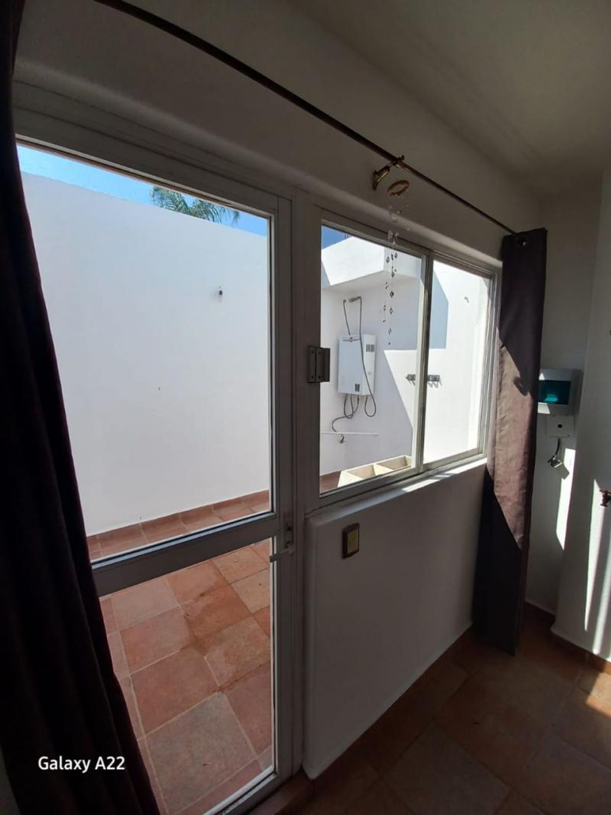 Puerta de cristal con marco blanco hacia patio exterior con piso de loseta terracota