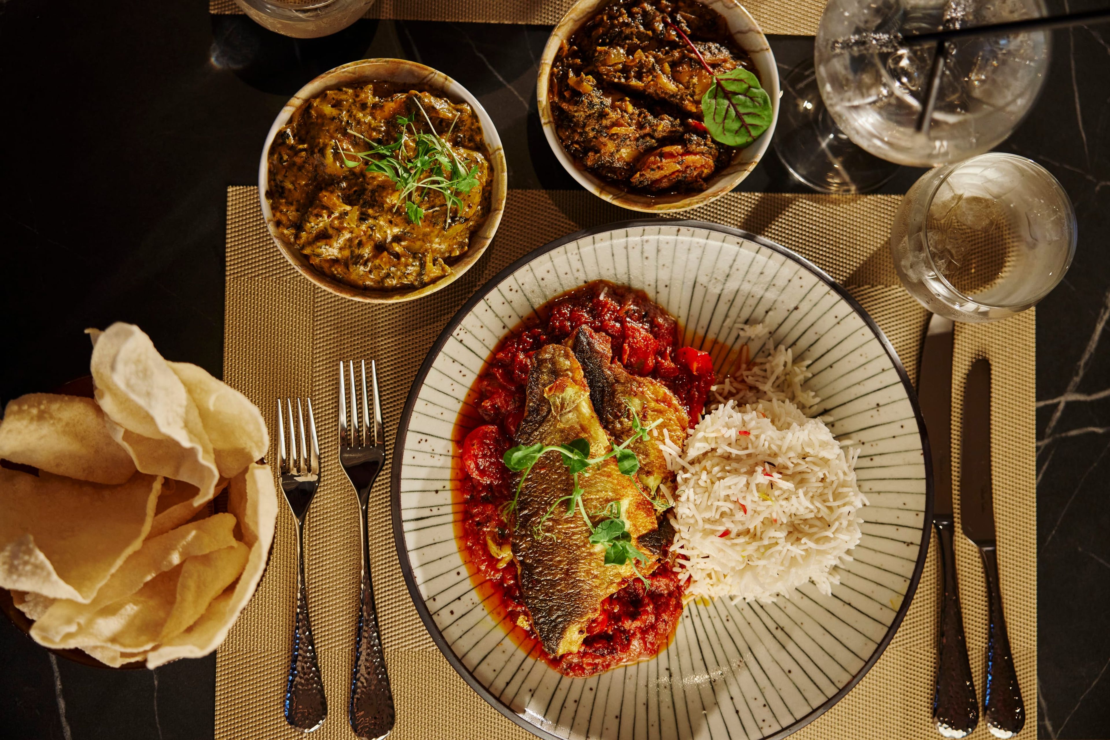 Pan-seared fish in a rich tomato sauce with rice, poppadoms and sides