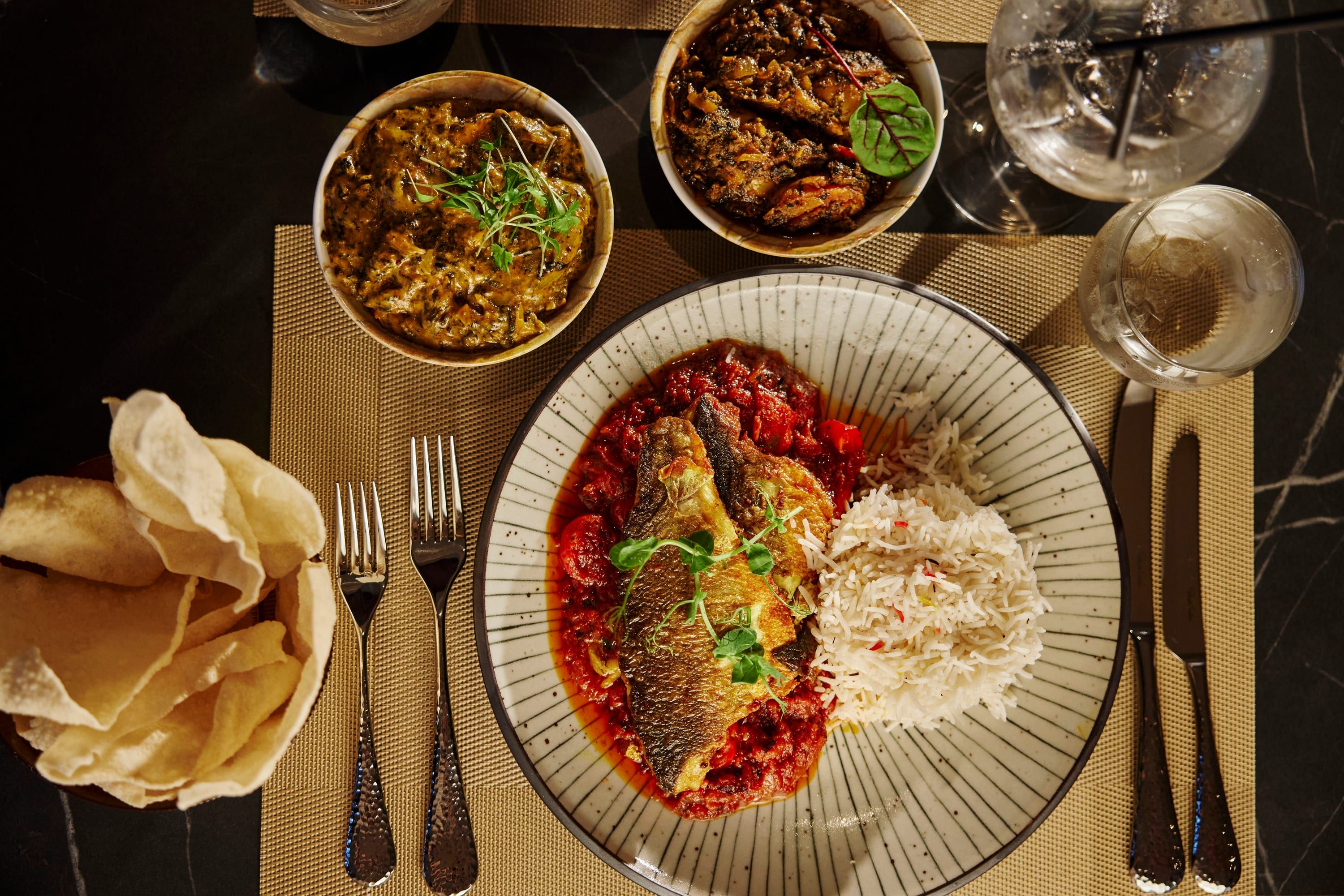 Pan-seared fish in a rich tomato sauce with rice, poppadoms and sides