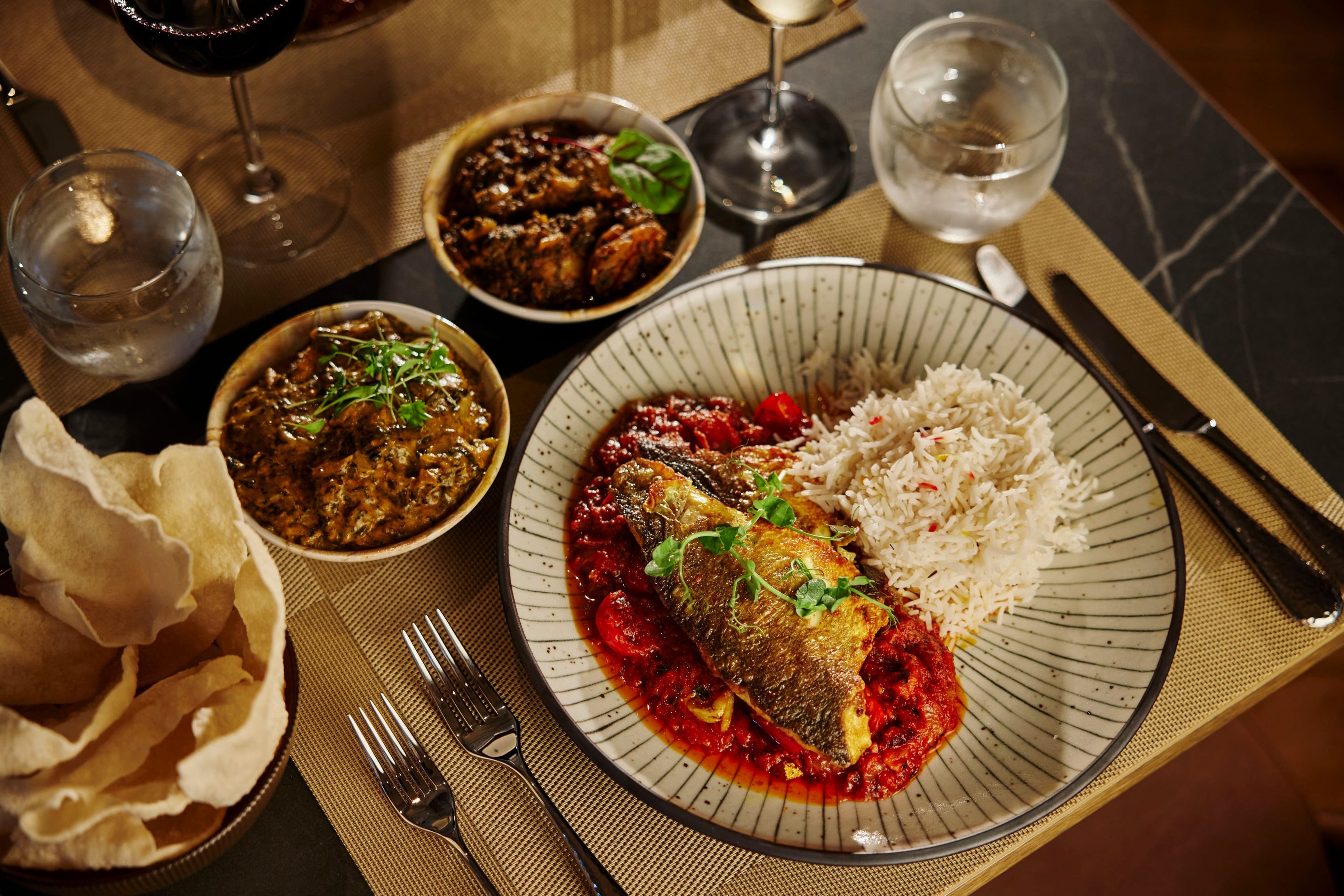 A spread of curries, rice, poppadoms and a fish dish on a marble table, seen from above