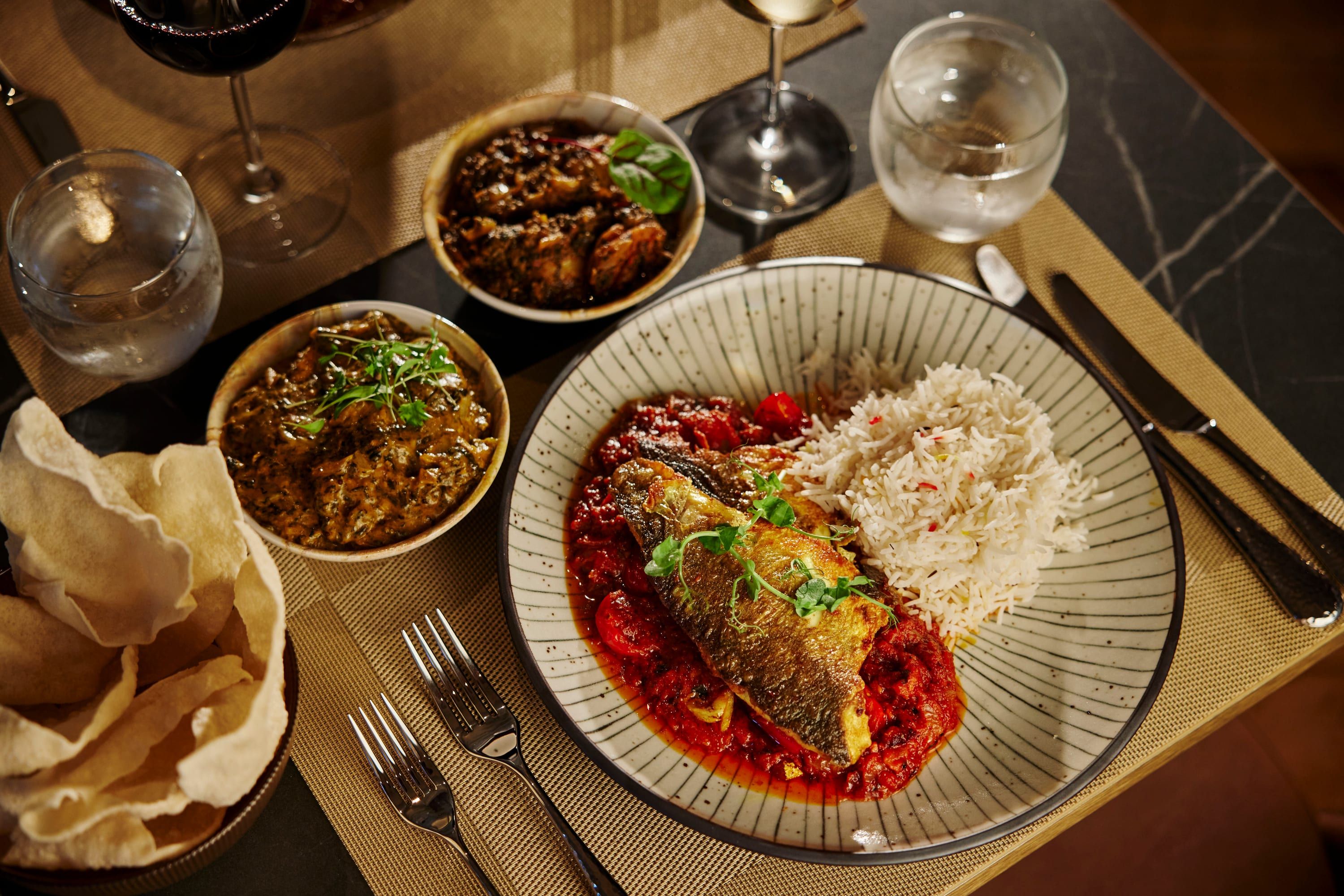A spread of curries, rice, poppadoms and a fish dish on a marble table, seen from above