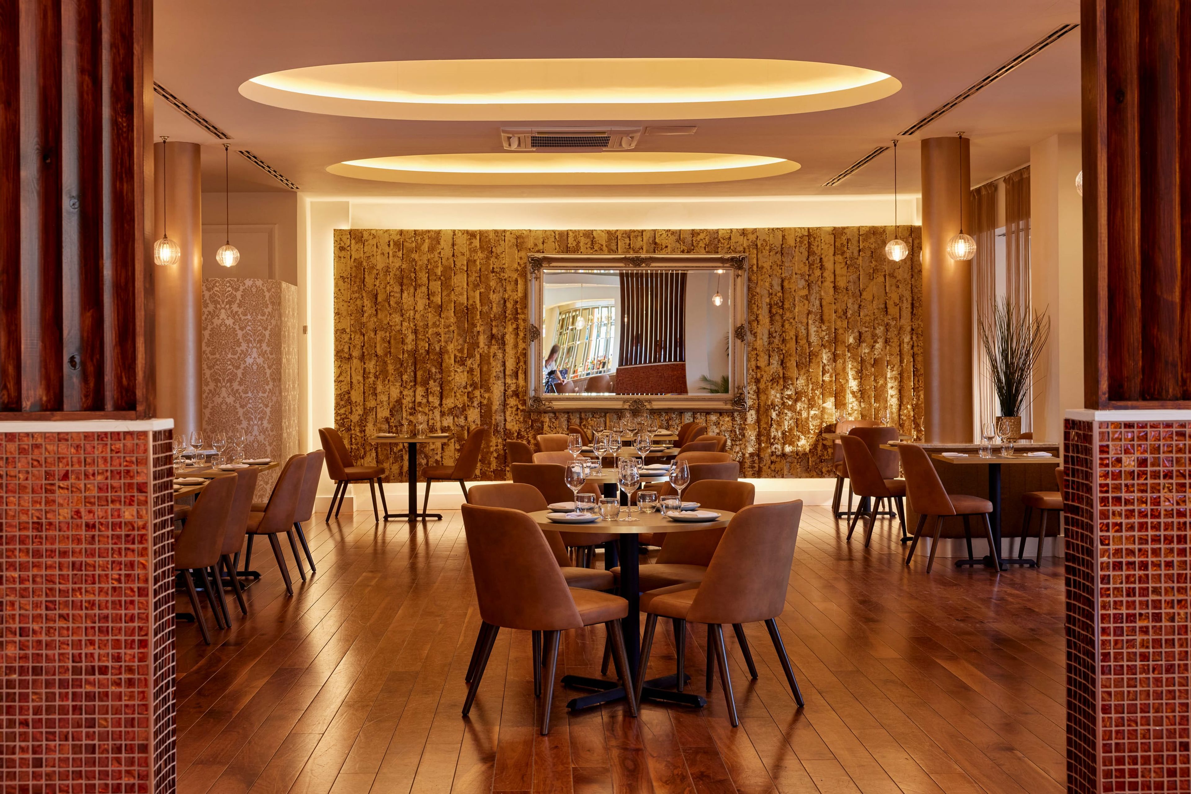 The SONA dining room between tiled columns, with round tables and a gilded feature wall