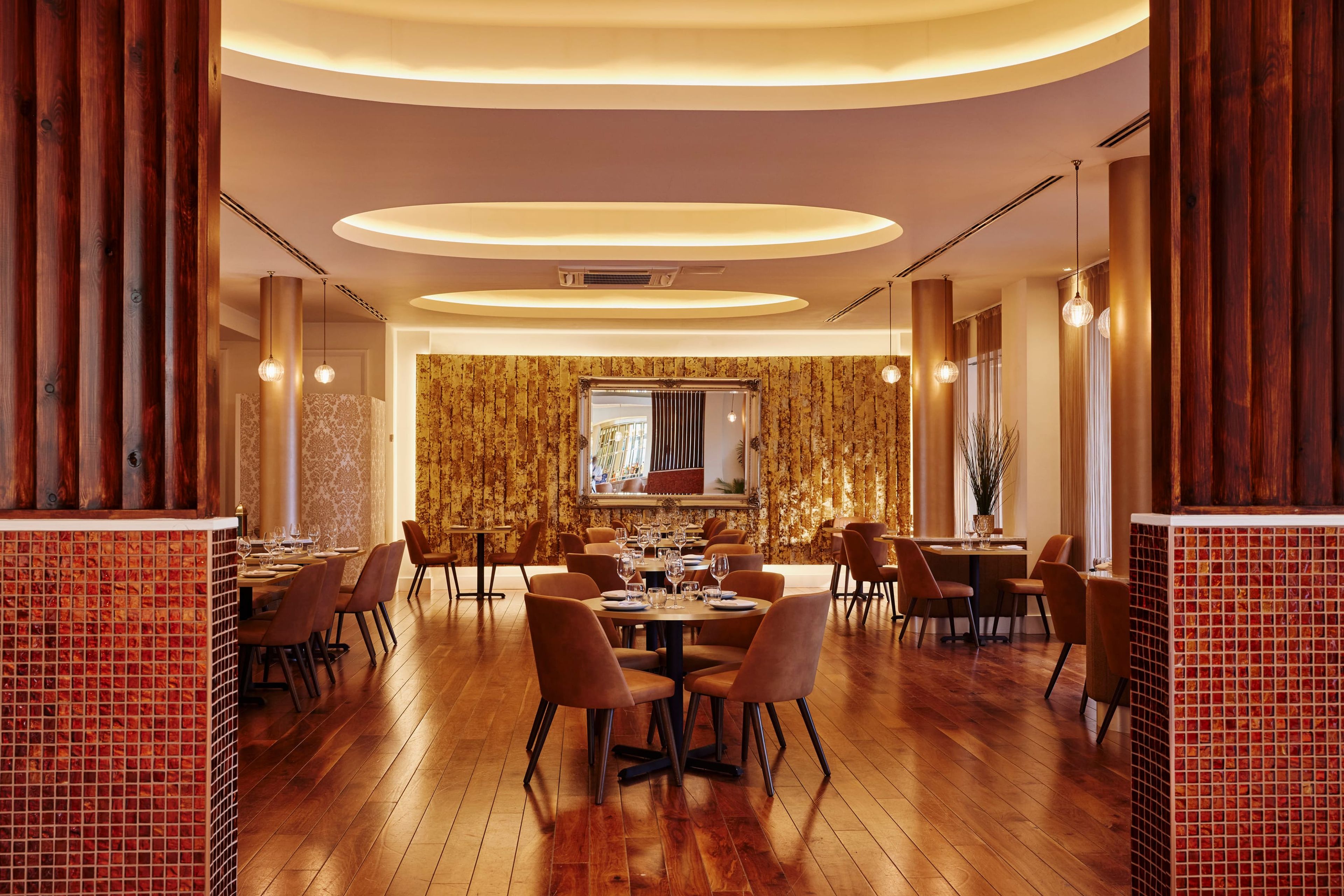 The SONA dining room seen between tiled columns, with round tables and a softly lit ceiling