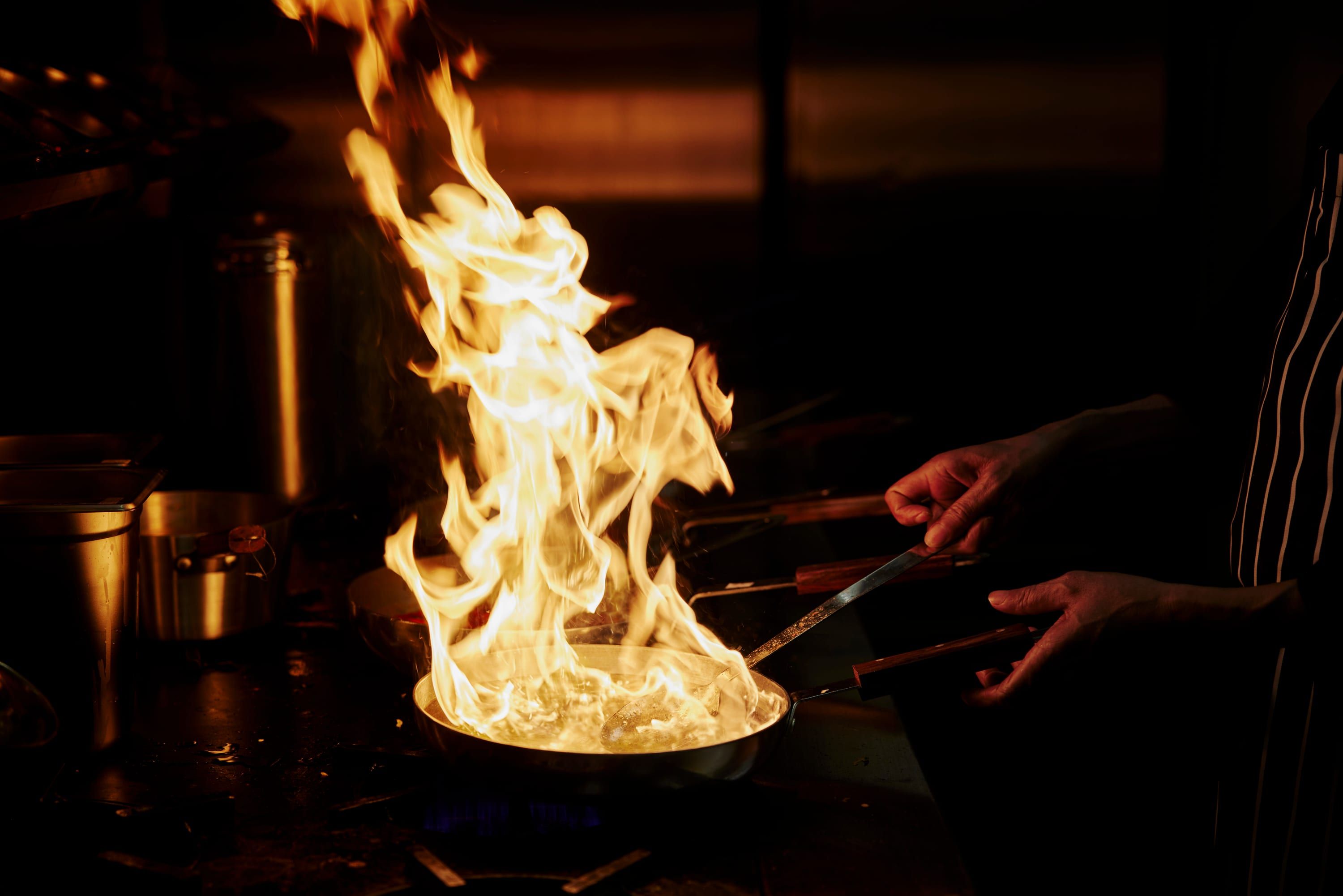 A chef flambéing a pan in the SONA kitchen, flames rising
