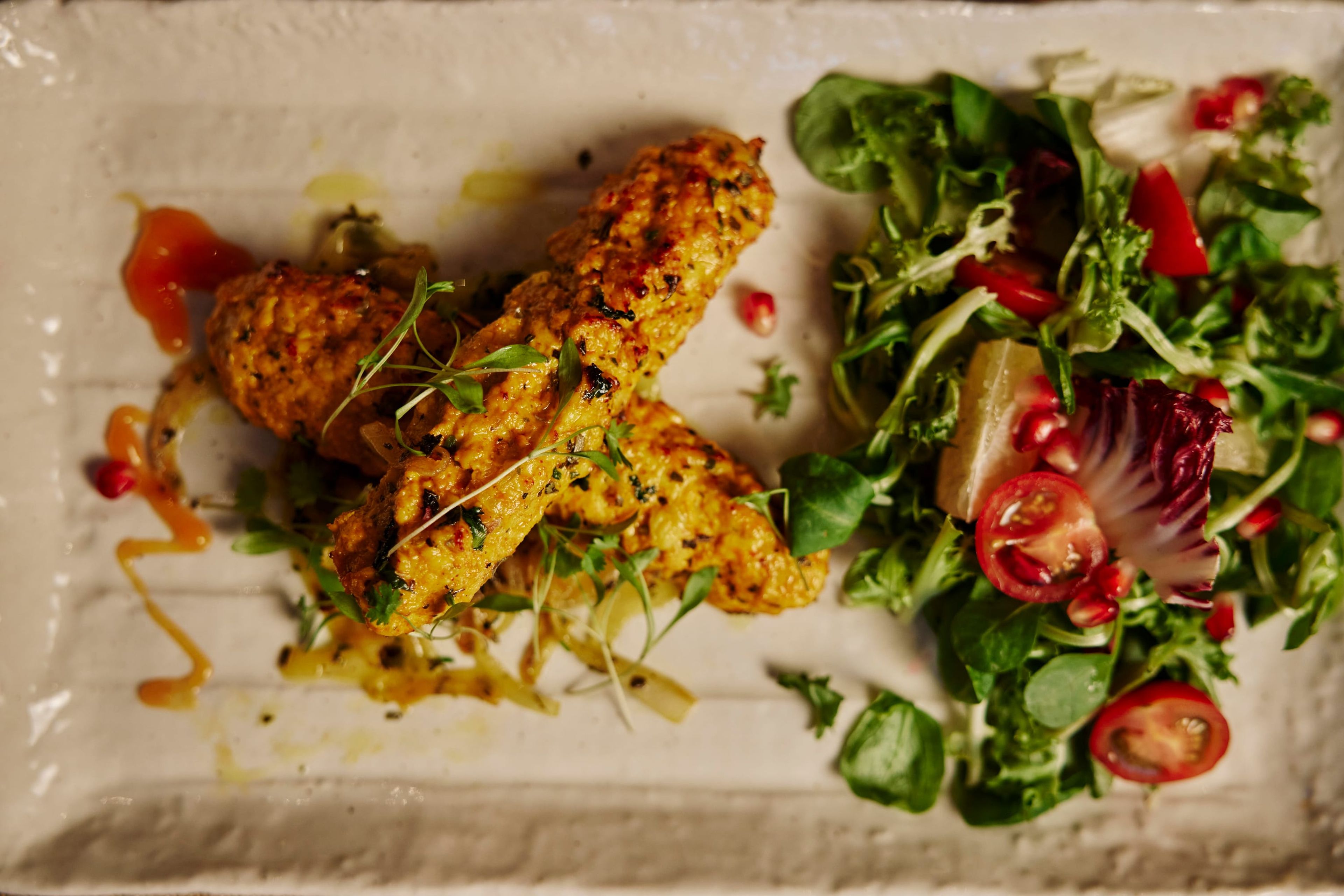 Chicken tikka with a pomegranate and leaf salad on a white plate