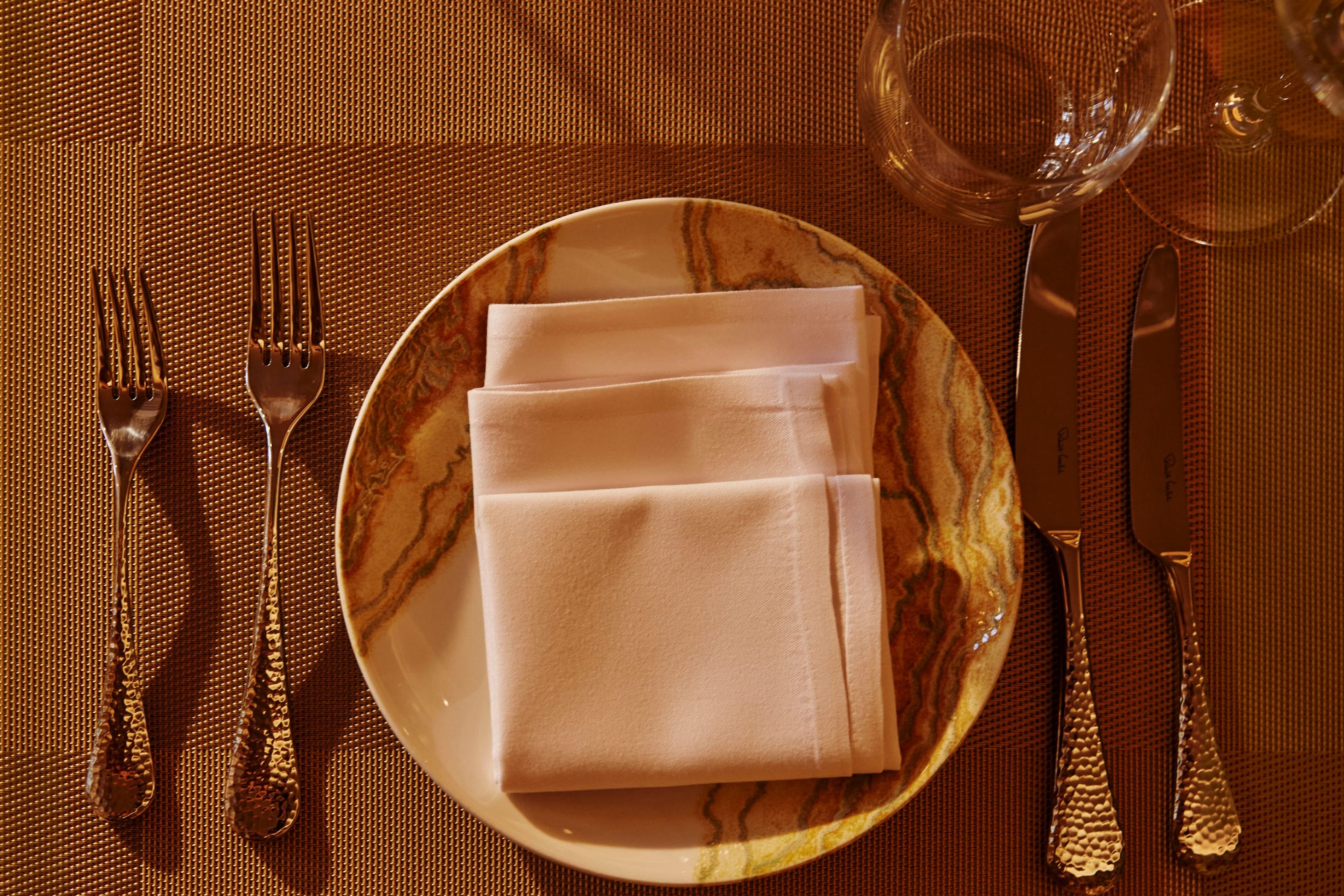 A SONA place setting from above: marble charger, folded napkin and engraved cutlery