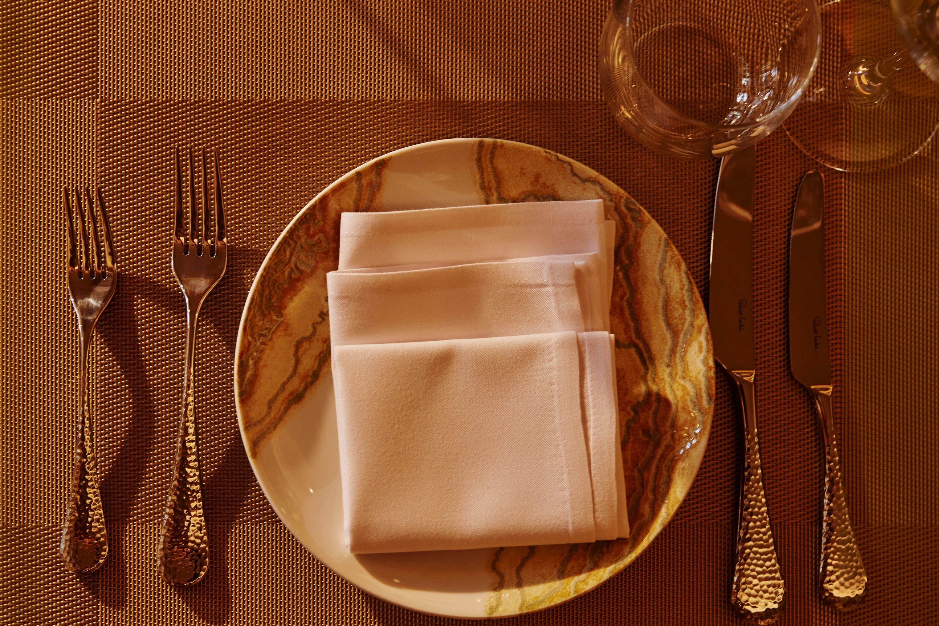 A SONA place setting from above: marble charger, folded napkin and engraved cutlery