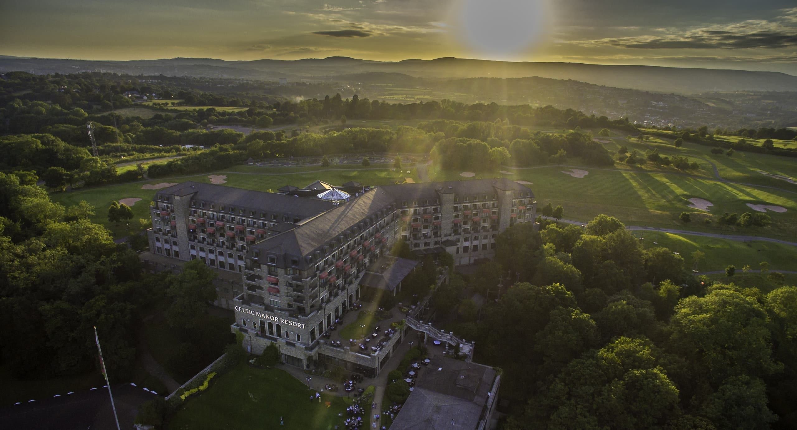 Aerial view of Celtic Manor Resort at sunset, surrounded by woodland and golf courses near Newport