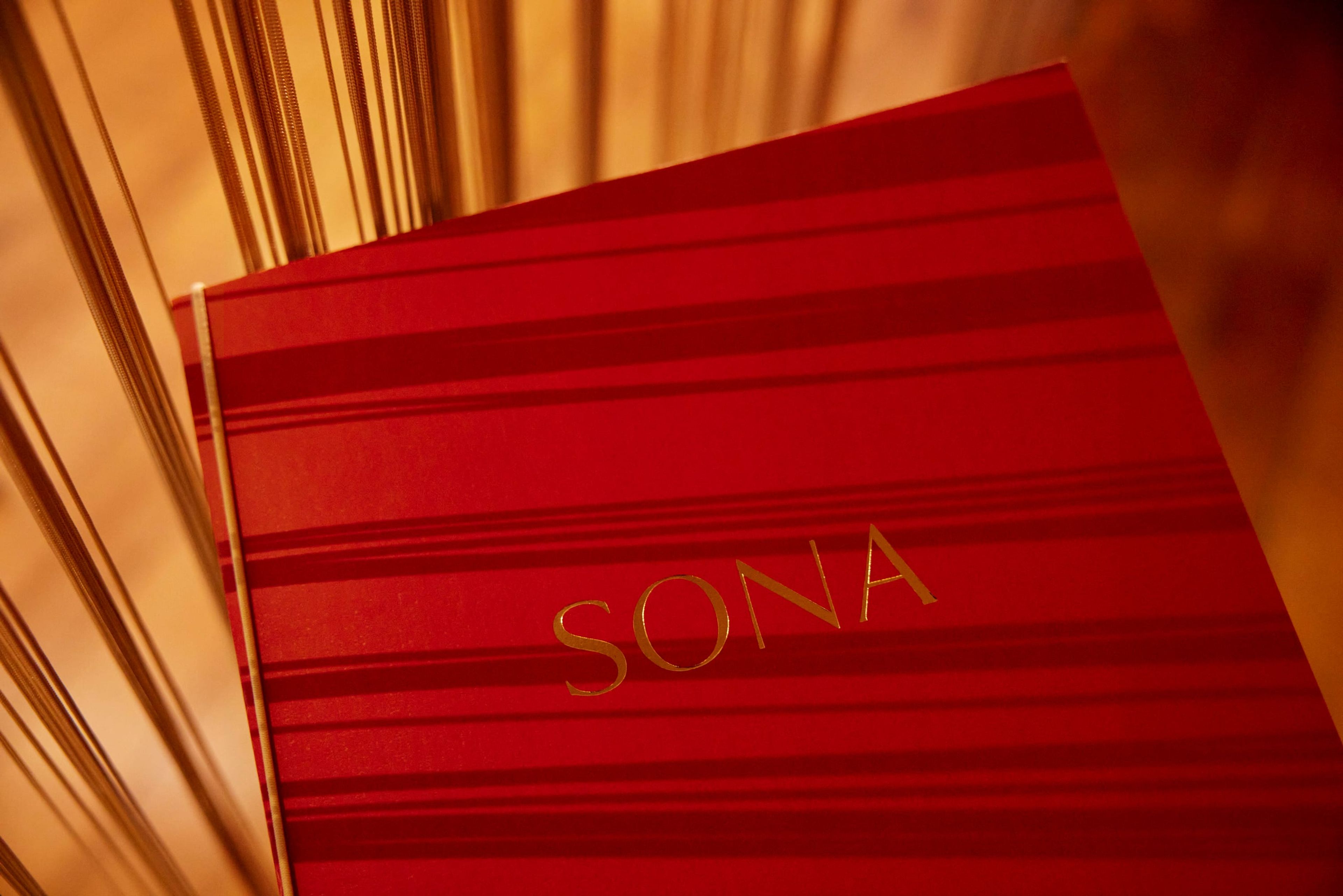 The red SONA menu book with gold lettering, lit by warm light