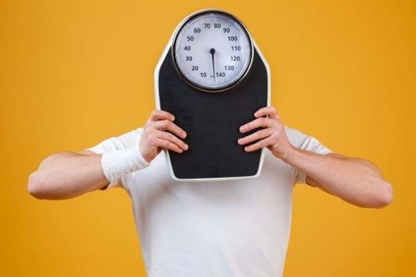 How to lose weight (and preserve strength) without doing cardio - picture: man holding scales in front of his face.