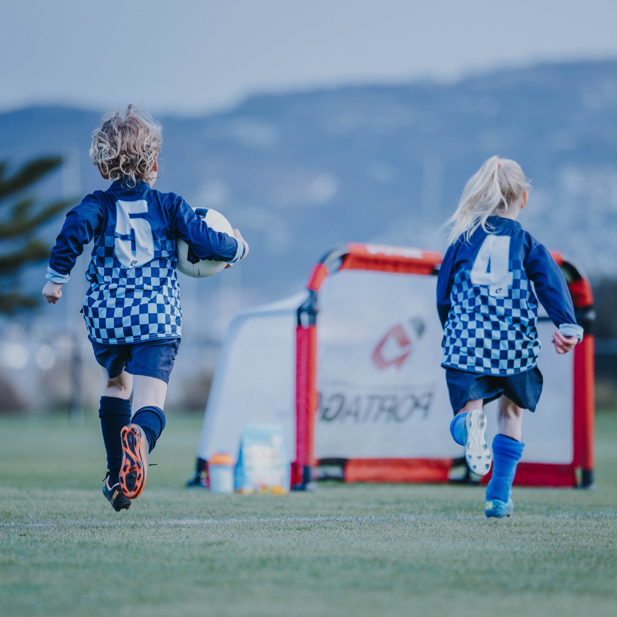 Two kids running towards the goals with Bulk Nutrients KidActiv beside