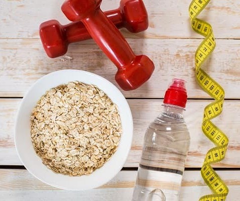 A bowl of oatmeal, two dumbbells, a drink bottle, and a body tape measure.