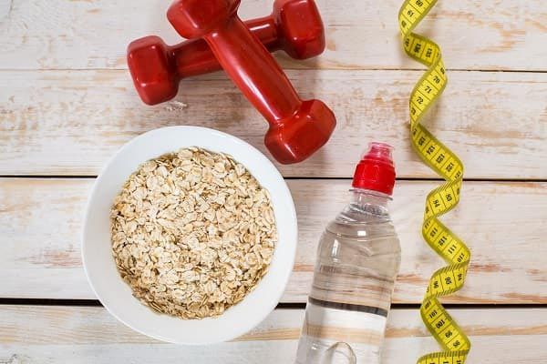 A bowl of oatmeal, two dumbbells, a drink bottle, and a body tape measure.