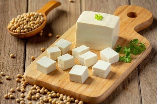 A wooden serving plate with a few nice chunk of tofu on it made from soybeans.