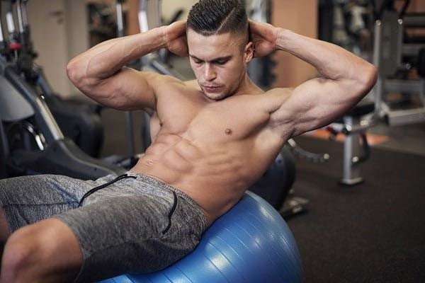 Muscular man performing sit ups on a yoga ball at the gym.